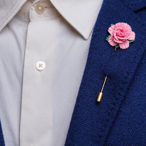 May include: A blue blazer with a white shirt and a pink flower lapel pin.