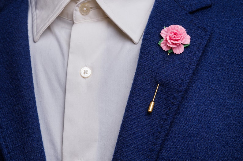 May include: A blue blazer with a white shirt and a pink flower lapel pin.