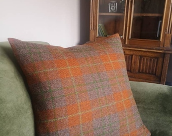 May include: A brown and orange plaid throw pillow with a green velvet sofa in the background.