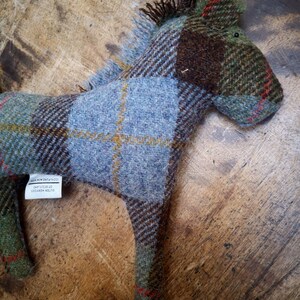 May include: A blue, green, and brown plaid horse toy made of wool. The toy has a tag that reads "Outer Hebrides,  of Scotland,  Made in Britain".