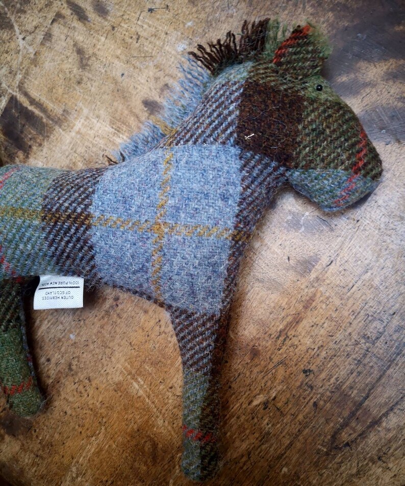 May include: A blue, green, and brown plaid horse toy made of wool. The toy has a tag that reads "Outer Hebrides,  of Scotland,  Made in Britain".