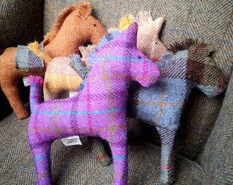 May include: Five plush toy horses made of tweed fabric in various colors, including purple, brown, yellow, and blue. The horses are sitting on a tweed armchair.