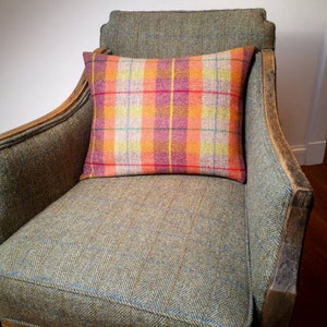 Puede incluir: Un sillón de tweed verde con un cojín a cuadros. El sillón tiene un marco de madera y un asiento acolchado.
