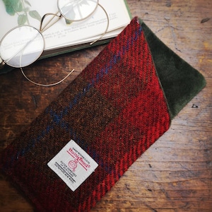 May include: A red and brown tweed eyeglass case with a green velvet lining. The case has a label that reads "Harris Tweed" and "Hand Woven Cloth."