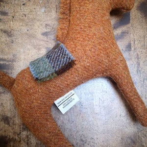 May include: A brown wool horse toy with a plaid saddle. The toy is handmade and has a tag that reads "OUTER HEBRIDES OF SCOTLAND  MADE IN THE UK  2808 MIN 780741205".