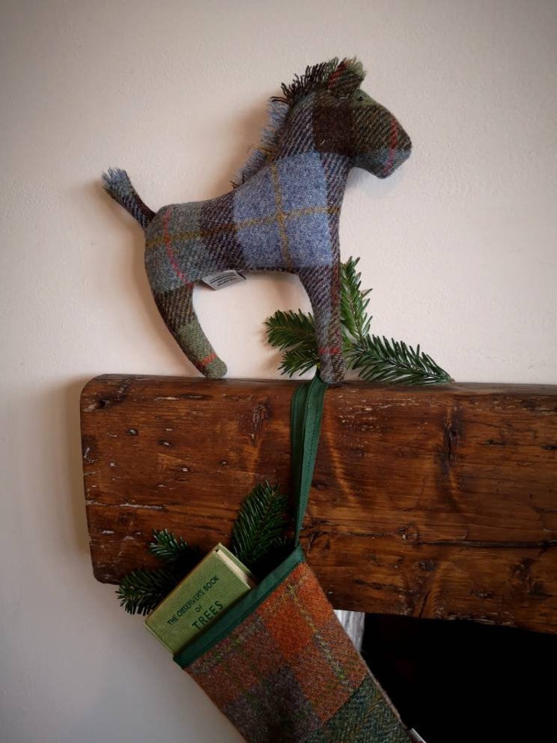 May include: A plaid stocking with a green ribbon hanging from a wooden mantel. A small book titled "The Observer's Book of Trees" is inside the stocking. A plaid horse figurine is perched on the mantel above the stocking.