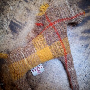 May include: A brown and yellow plaid horse toy with red accents. The toy is made of wool and has a label that says "Harris Tweed" on it.
