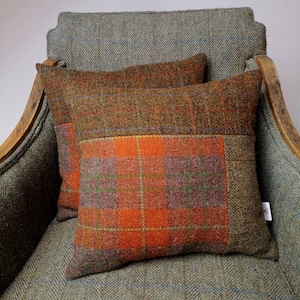 May include: Two throw pillows with a brown, orange, and green plaid pattern. The pillows are on a green and blue tweed armchair.