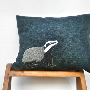 May include: A dark blue throw pillow with a white and gray embroidered badger design.