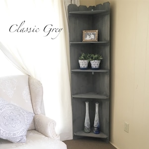 May include: A corner shelf unit with four shelves in a classic grey finish. The shelves are decorated with potted plants, vases, and a framed photo.