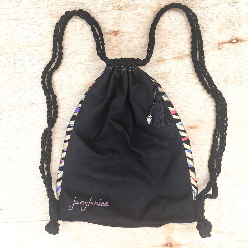 May include: Black drawstring bag with a geometric pattern in gold, blue, and pink. The bag has a black tassel and the text "junglenice" is embroidered on the front.