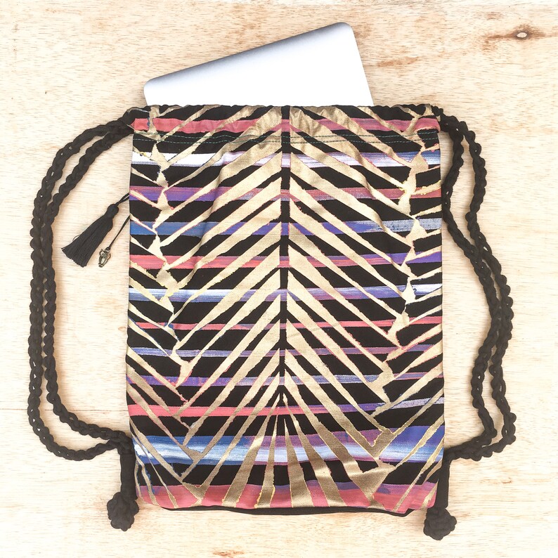 May include: A black drawstring backpack with a gold, pink, and blue geometric pattern. The backpack has a laptop inside and a black tassel on the drawstring.