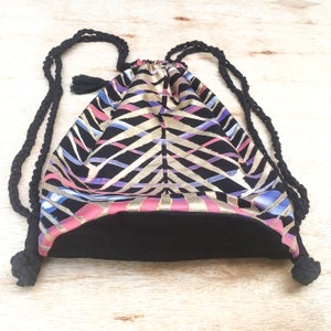 May include: A black drawstring bag with a geometric pattern in shades of pink, gold, and blue. The bag has black drawstrings and a black lining.