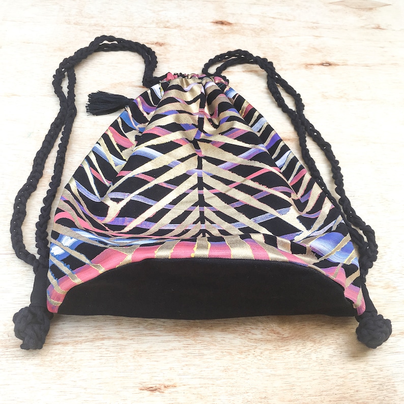 May include: A black drawstring bag with a geometric pattern in shades of pink, gold, and blue. The bag has black drawstrings and a black lining.