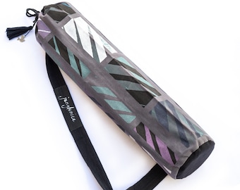 May include: A gray yoga mat bag with a black strap and a geometric pattern in shades of teal, purple, and white. The bag has a drawstring closure and a small tassel. The text "JungJanice" is printed on the strap.