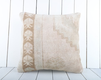 May include: A beige throw pillow with a geometric pattern and a border of stylized floral motifs. The pillow is made of a soft, woven fabric and has a slightly distressed look.