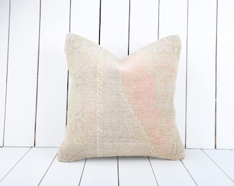 Puede incluir: Una almohada cuadrada con tejido blanco roto. La almohada tiene un sutil patrón rosa y gris descolorido.