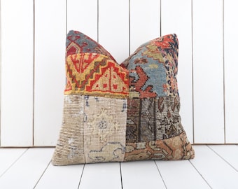 Puede incluir: Un cojín patchwork con una variedad de colores y patrones. El cojín presenta secciones de telas rojas, doradas, azules y beige, creando un diseño único y texturizado. El cojín es un artículo decorativo.