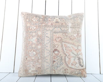 May include: A square throw pillow with a beige background and a floral pattern in shades of pink and gray. The pillow has a fringe border.