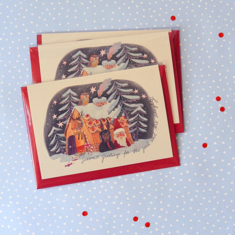 May include: A set of three Christmas cards featuring a gingerbread house with a snowy roof, surrounded by trees and a group of characters including Santa Claus, a devil, and an owl. The cards have a red border and the text "Seasons Greetings for the good and the naughty".