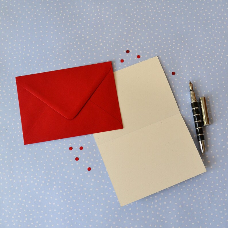 May include: A red envelope with a blank white card inside. A black pen is lying on the card. The card and envelope are on a blue background with white polka dots.