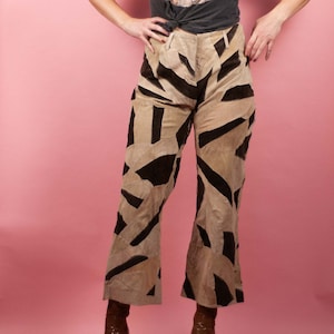 May include: A woman wearing a gray t-shirt with a band graphic and brown patterned pants. She is wearing brown boots and has a black headband in her hair.