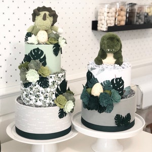 Peut inclure: Deux g&acirc;teaux de couches d&eacute;cor&eacute;s de dinosaures en peluche, de plantes succulentes en feutrine et de feuilles de monstera. Le g&acirc;teau de gauche a trois &eacute;tages en tissu vert clair, imprim&eacute; botanique et gris. Celui de droite a deux &eacute;tages gris et blanc.
