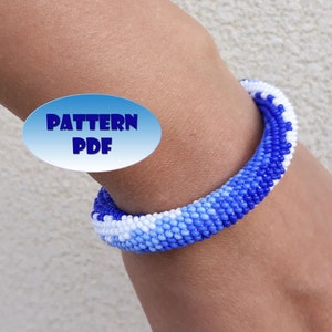Op de afbeelding: Een blauwe, witte en lichtblauwe kralen armband met een verloop patroon. De armband zit om de pols van een persoon. De tekst "PATTERN PDF" staat op een blauwe ovale sticker.