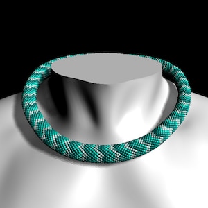 Puede incluir: Un collar de cuentas turquesa y blanco con un patrón geométrico. El collar está hecho de pequeñas cuentas redondas que están enhebradas en un diseño en espiral.