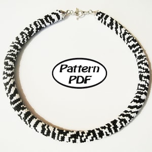 May include: Black and white beaded necklace with a zebra print pattern. The necklace is made with small beads and has a silver clasp.