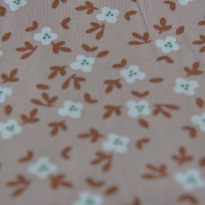 May include: A close-up of a light pink fabric with a repeating pattern of small white flowers and brown leaves.