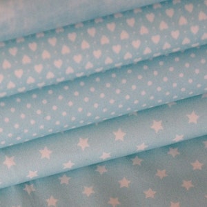 Pode incluir: Quatro peças de tecido azul claro com diferentes padrões brancos. Os padrões incluem corações, pontos e estrelas.