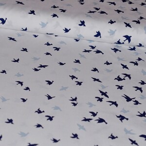 May include: White fabric with a repeating pattern of dark blue bird silhouettes. The birds are scattered randomly across the fabric.