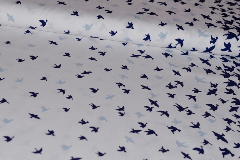 May include: White fabric with a repeating pattern of dark blue bird silhouettes. The birds are scattered randomly across the fabric.