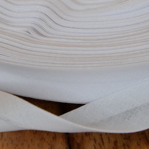 Puede incluir: Un rollo de cinta de bies blanca, un tipo de adorno de tela que se utiliza para terminar los bordes de la tela.