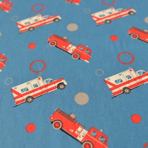 May include: Blue fabric with a repeating pattern of red and white fire trucks and ambulances. The background is dotted with red and gray circles.