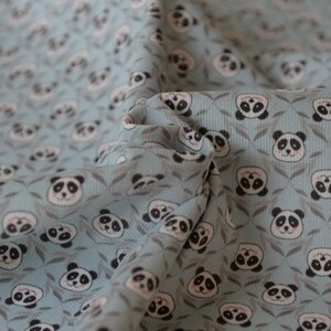 K&ouml;nnte beinhalten: Ein blauer Stoff mit einem sich wiederholenden Muster von Pandab&auml;ren-Gesichtern. Die Pandas sind wei&szlig; mit schwarzen Augen und Ohren und von kleinen gr&uuml;nen Bl&auml;ttern umgeben.