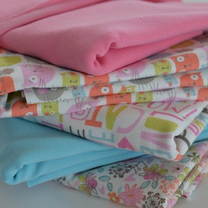 Könnte beinhalten: Ein Stapel Stoffreste in verschiedenen Farben und Mustern, darunter rosa, blau, weiß und ein Katzenmuster. Die Stoffreste sind gefaltet und übereinander gelegt.