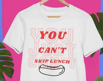 May include: White t-shirt with the text "You Just Can't Skip Lunch" in red and pink letters. A black and white outline of a hot dog with mustard is below the text.