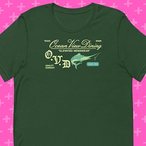 May include: A dark green t-shirt featuring the text "Ocean View Dining" and a marlin graphic. The shirt also includes the text "O.V.D." and "Since 1982". The shirt is made of a soft material.