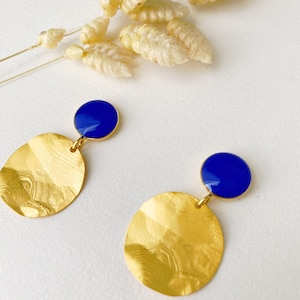 以下が含まれることがあります： テクスチャ加工が施されたハンマー仕上げのゴールドイヤリングのペア。各イヤリングには、小さな丸い青い石がセットされています。