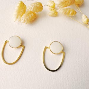 Peut inclure: Une paire de boucles d'oreilles en or avec des pierres circulaires blanches. Les boucles d'oreilles ont un design simple et moderne.