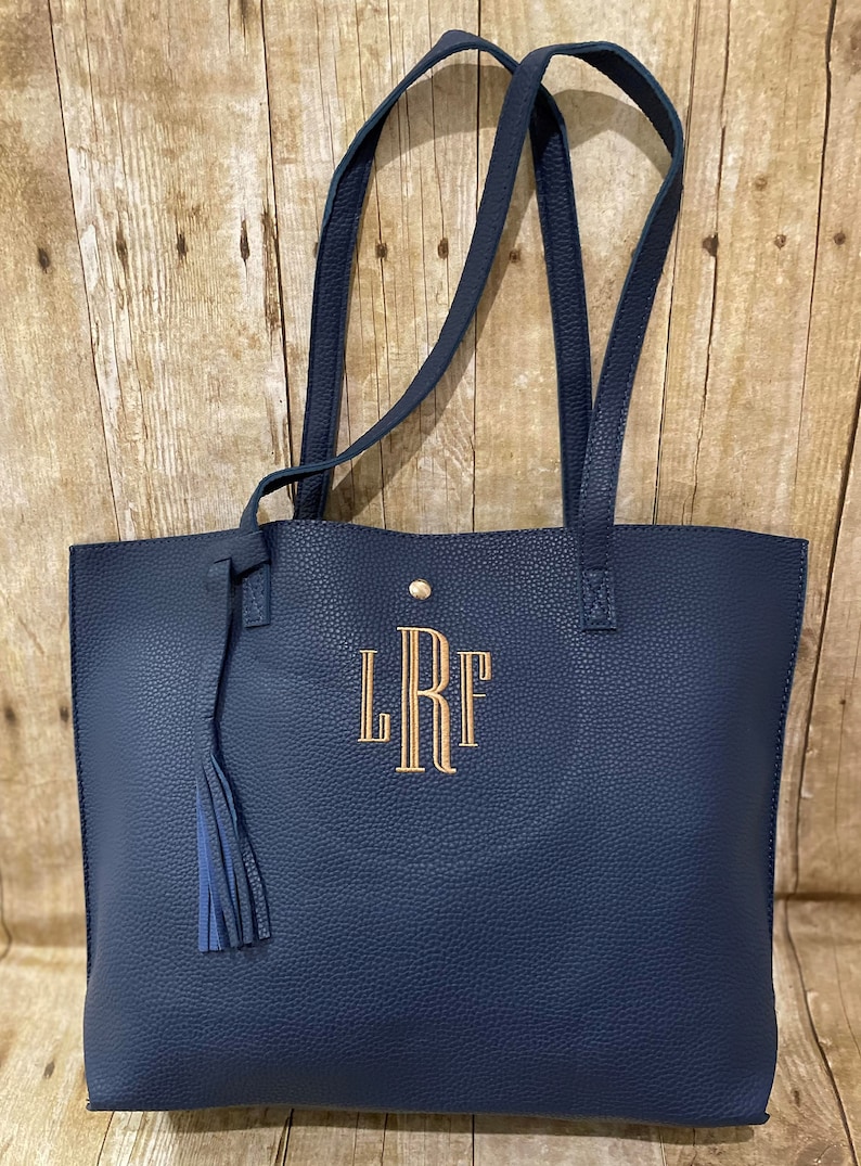 Op de afbeelding: Een donkerblauwe tote bag met een gouden kwast en gemonogrammeerd met de initialen "LRF".