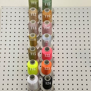 Op de afbeelding: Een wand met spoelen garen in verschillende kleuren, genummerd van 111 tot 124.