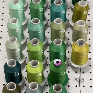 Op de afbeelding: Een wanddisplay met 18 spoelen groene, blauwe en gele draad. De spoelen zijn genummerd van 26 tot en met 47.