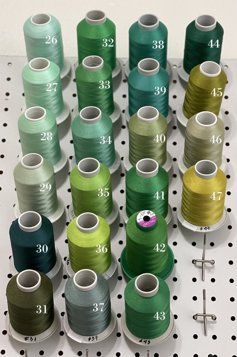 Op de afbeelding: Een wanddisplay met 18 spoelen groene, blauwe en gele draad. De spoelen zijn genummerd van 26 tot en met 47.