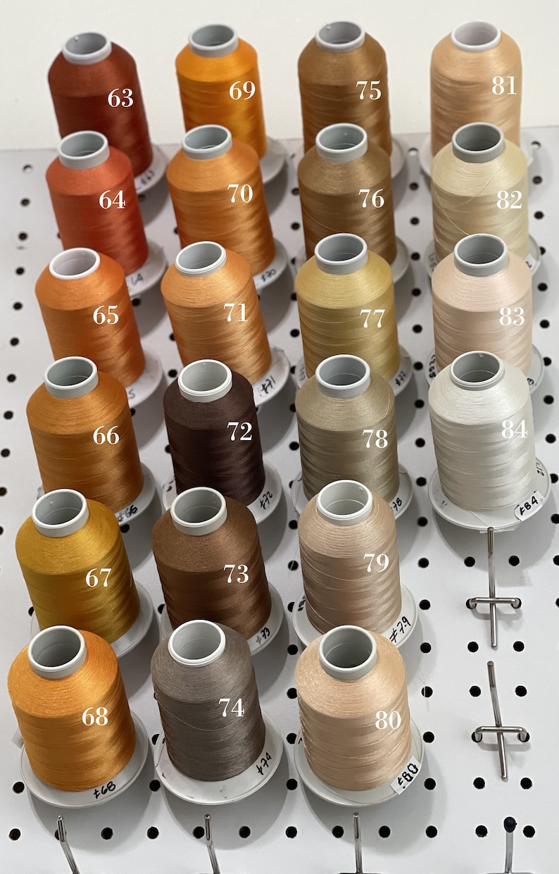 Op de afbeelding: Een wanddisplay met 20 spoelen garen in verschillende tinten bruin, oranje en beige. De spoelen zijn genummerd van 63 tot en met 84.