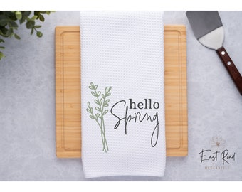 May include: White kitchen towel with a green floral design and the text "hello spring" in black script.
