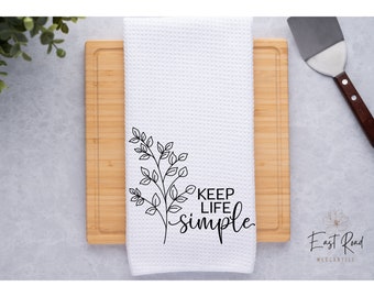 May include: White kitchen towel with a black floral design and the text "Keep life simple".