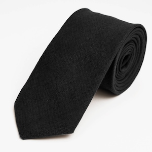 Peut inclure: Une cravate noire en tissu texturé. La cravate est enroulée et prête à être portée.
